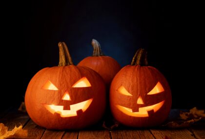 Two pumpkins on a table. They have scary faces carved into them.